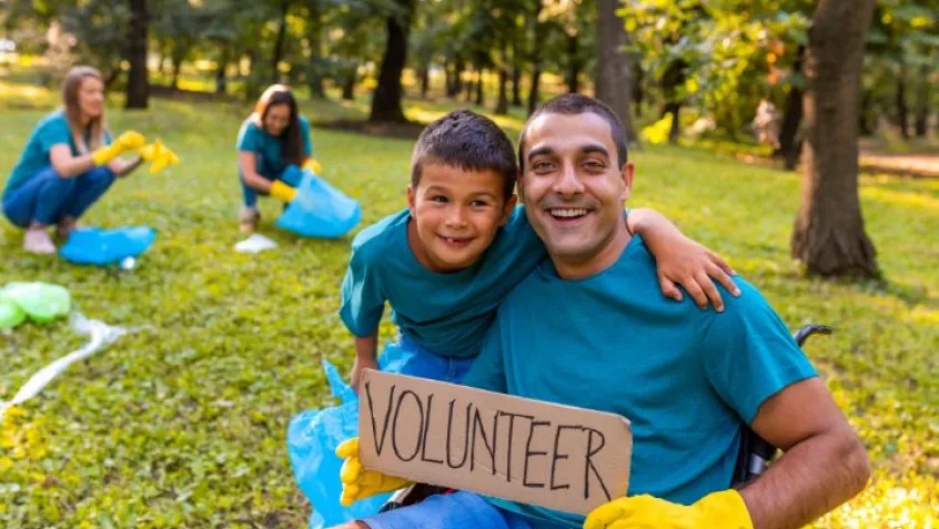 a father and son outdoors holding a sign that says volunteer during a clean up