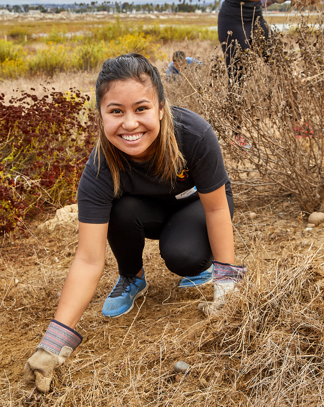 Young woman with gloves smiling and removing weeds