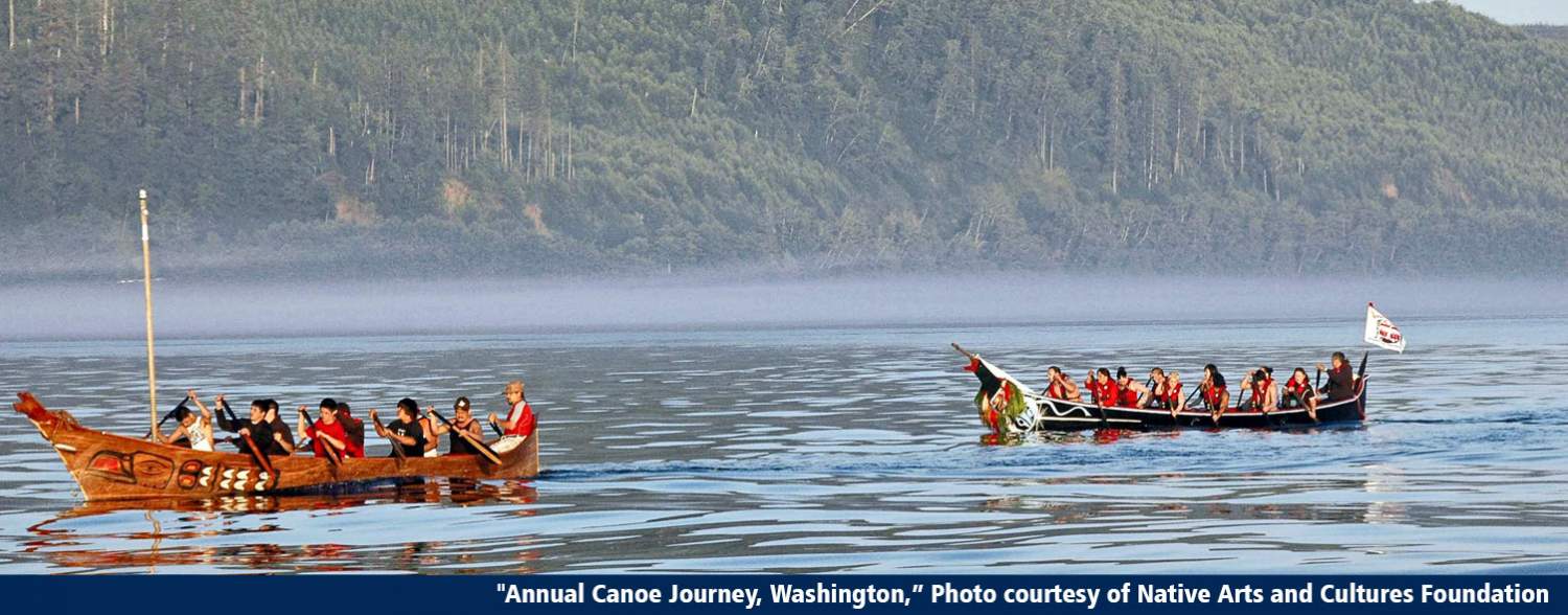 two long Native American boats filled with people rowing sail along a river with mountains in the background.