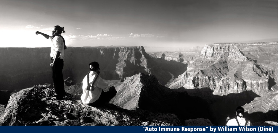 a black and white photo of two Native American men with gas masks on standing at the top of a canyon, one has his fist raised.