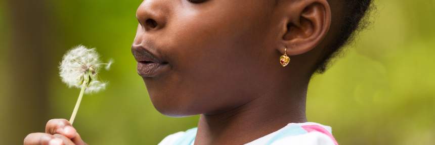 a young girl blows on a dandelion 