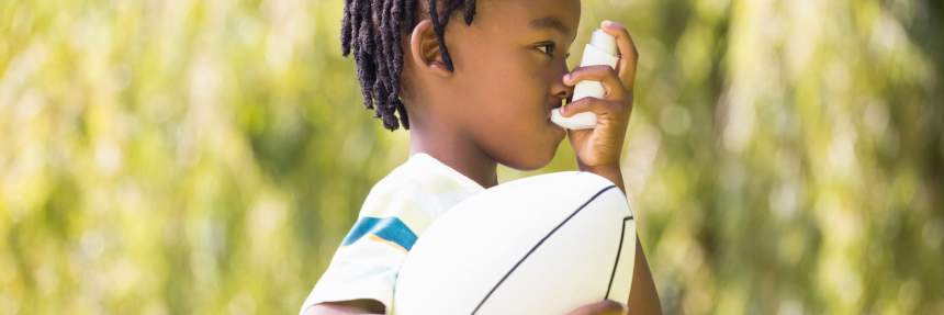 young boy using an asthma inhaler while holding a football