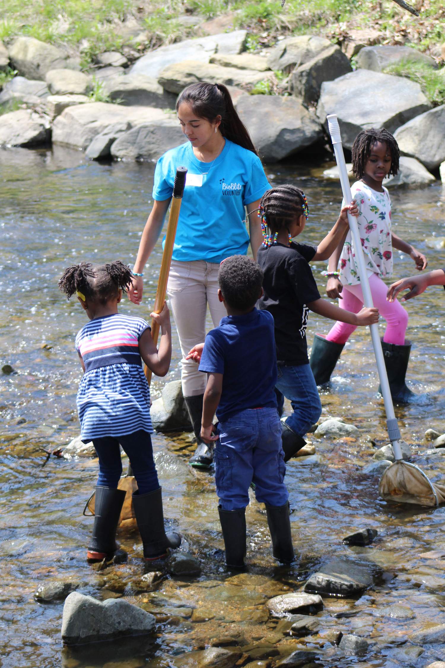 Children and group activity leader in river walking on rocks