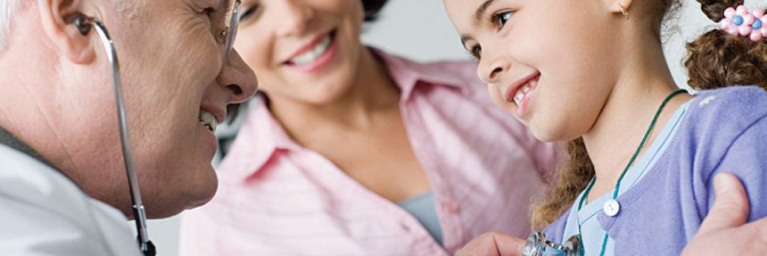 doctor using a stethoscope to listen to the heart of a young girl with mother in the background