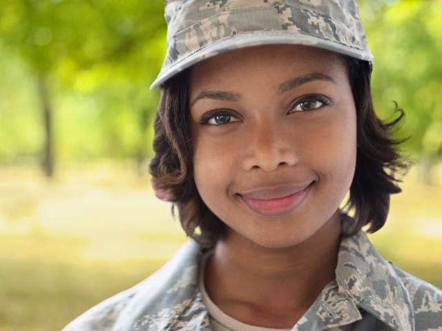 Young woman in camouflage hat and jacket, veteran, looking at the camera and smiling.