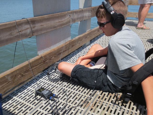 Young man with headphones sitting on a dock with a recording device