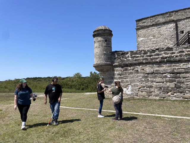 Young people with recording devices outside near a stone building