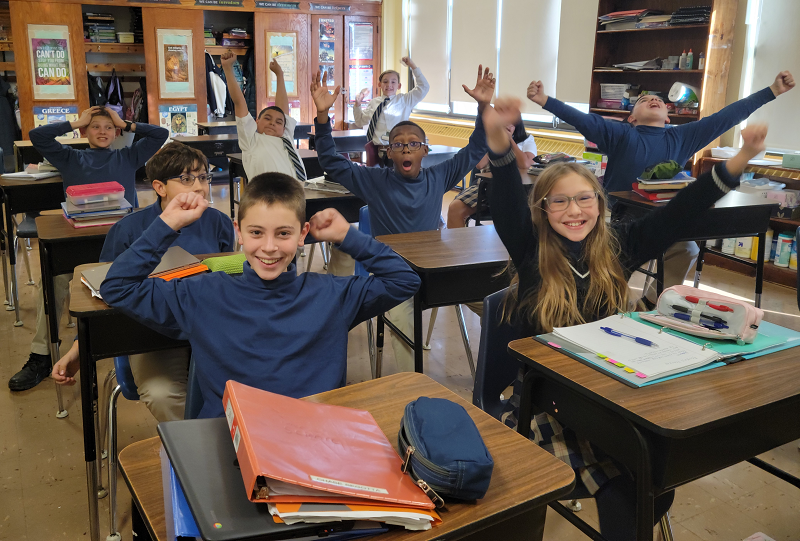 Students at desks with their hands in the air
