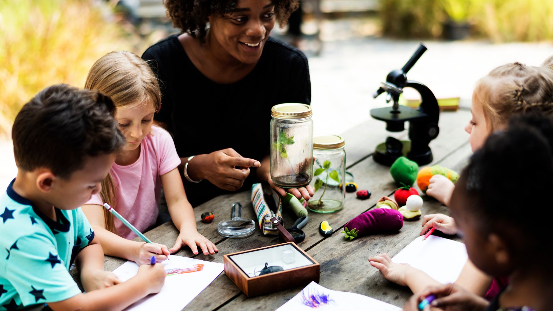 an environmental educator holds a seedling in a jar as part of an environmental education lesson with some students