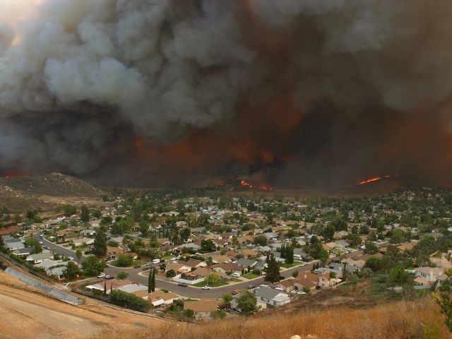 a wildfire in California releases plumes of smoke into the air near a community of homes