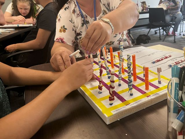 A student and teacher are seated at a table, working together on an arts and crafts project exploring the water cycle.