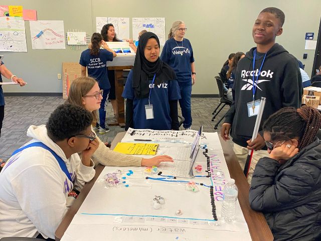 Five students stand around a table covered in charts they created to measure the water cycle.