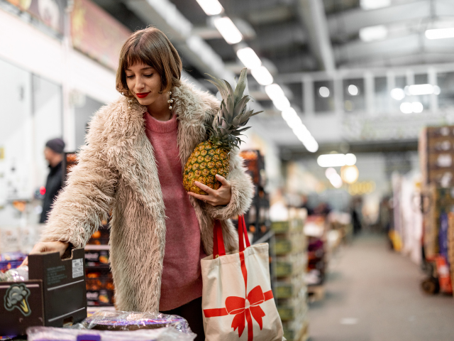 a woman in a store holds a pineapple and a reusable holiday bag