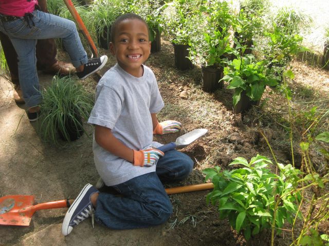 A young boy smiles as he prepares the soil for planting during a volunteering event.