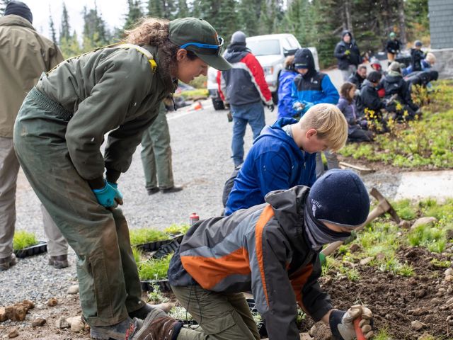 a park staff member instructs youth at a volunteering event outdoors
