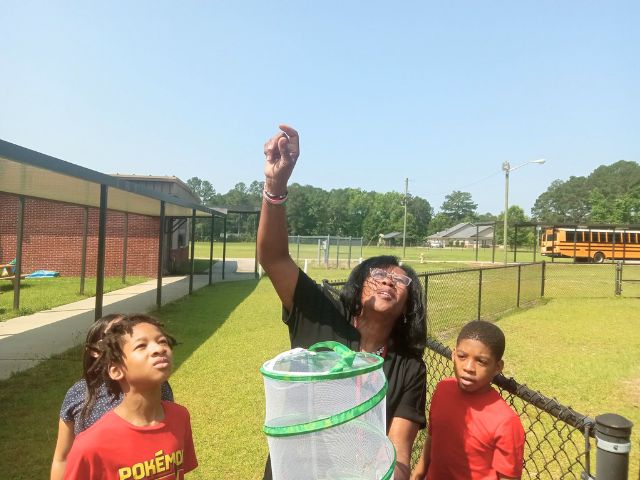 Students stand with a teacher as they release a pollinator as part of a science project.