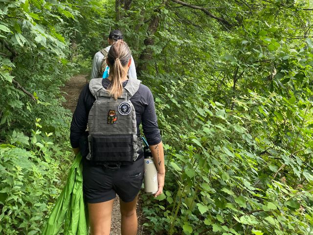 a woman and a man hike through the forest with a military style backpack