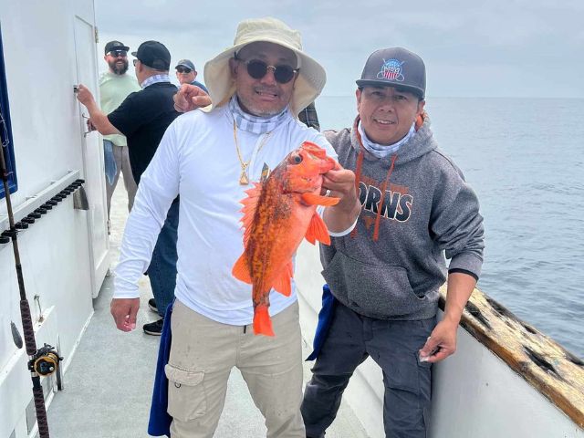 two military veterans stand on a boat, one holds a fish