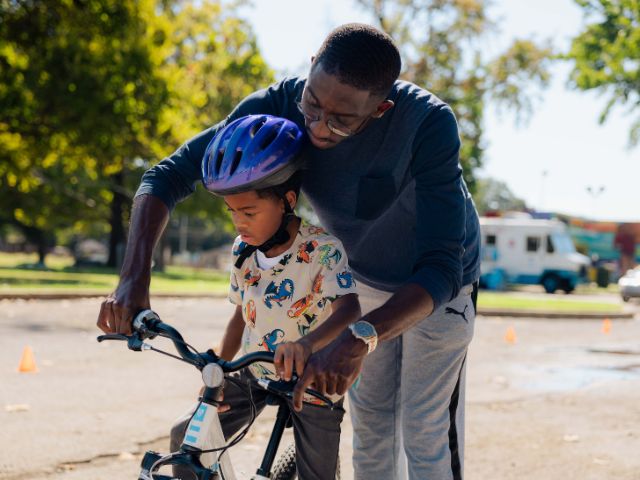 a father helps his son ride a bike during an NPLD Bike Rodeo a Gooch Park.