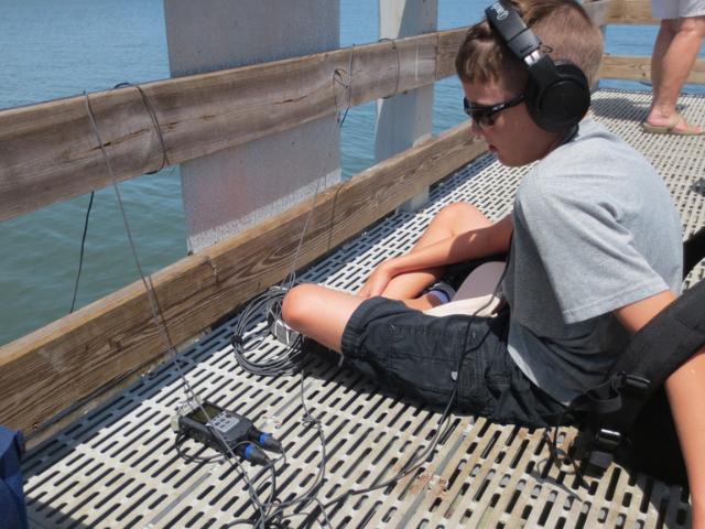 Boy with headphones on using audio equipment on pier. Canaveral National Seashore, Atlantic Center for the Arts