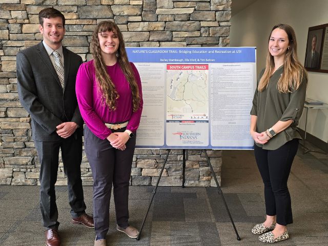 students from University of Southern Indiana stand near a poster of their Nature Classroom project