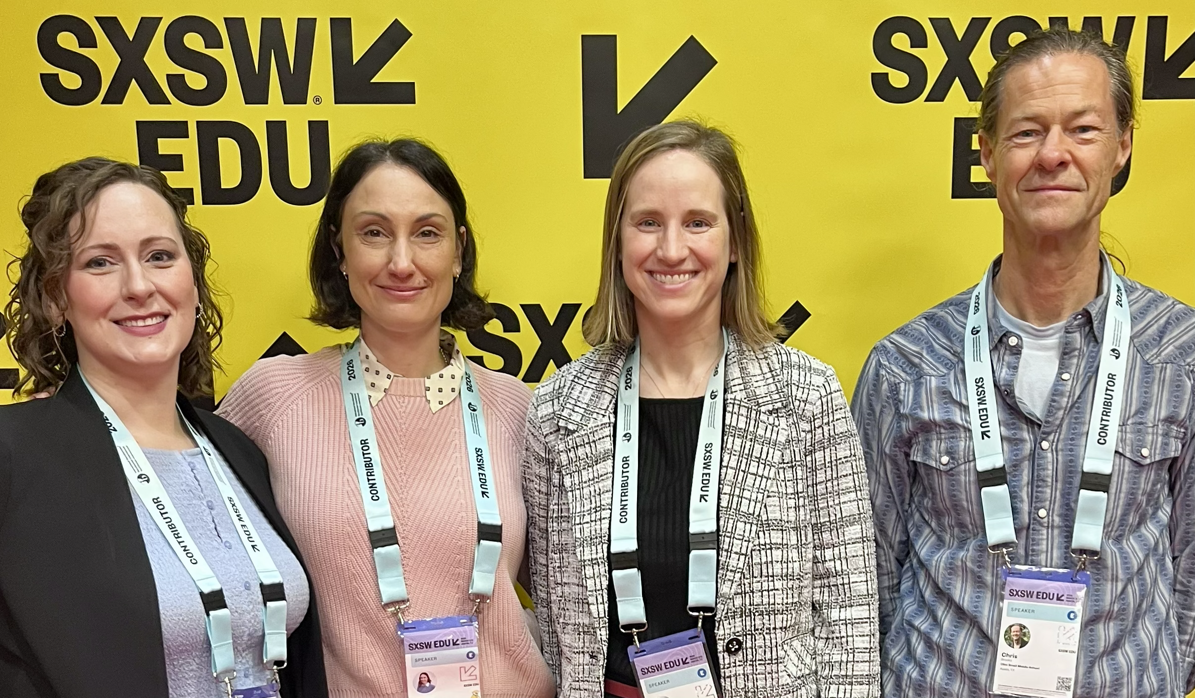Four people standing in front of a yellow sign smiling