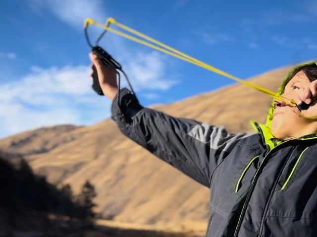 A volunteer uses a slingshot to disperse seedballs across a river