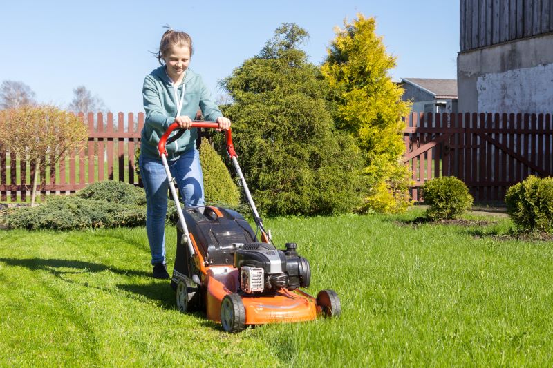 Woman mowing the grass a fenced in yard with trees and shrubs