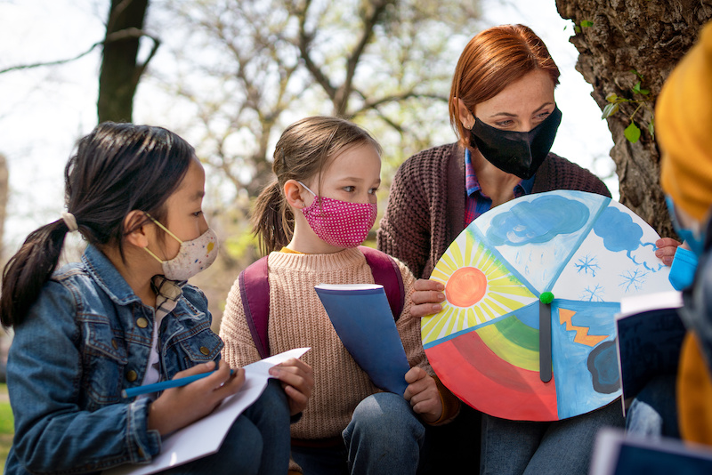 Students in the outdoors with masks on learning from a teacher
