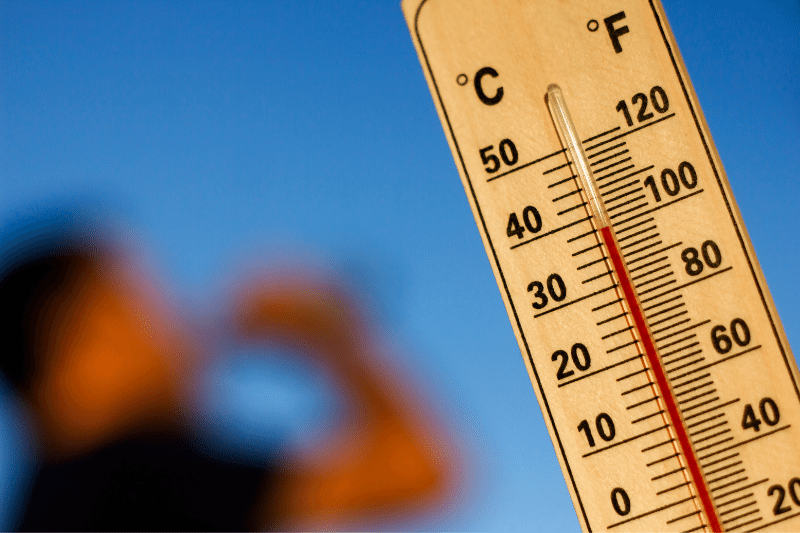 thermometer reading 100 degree F with a blurred photo of person drinking water 