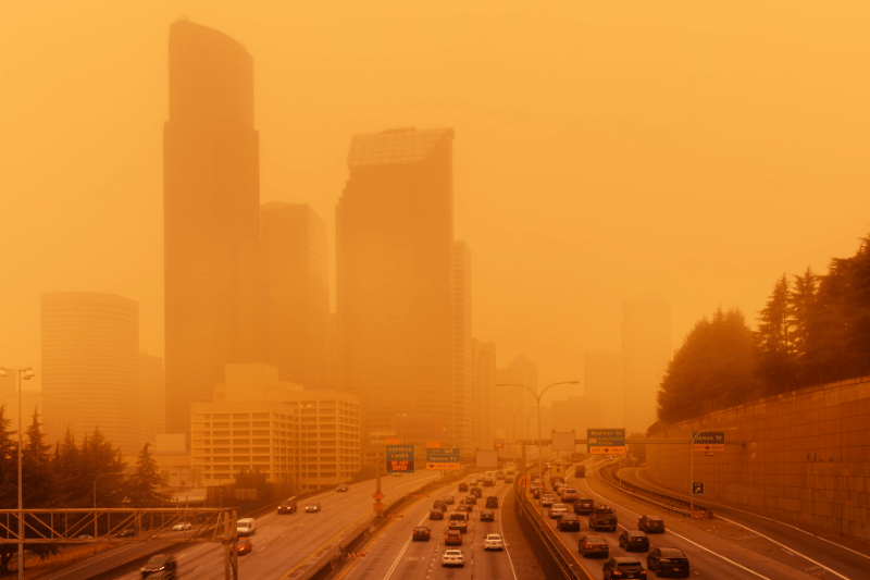 wildfire smoke over a highway with city skyline in background