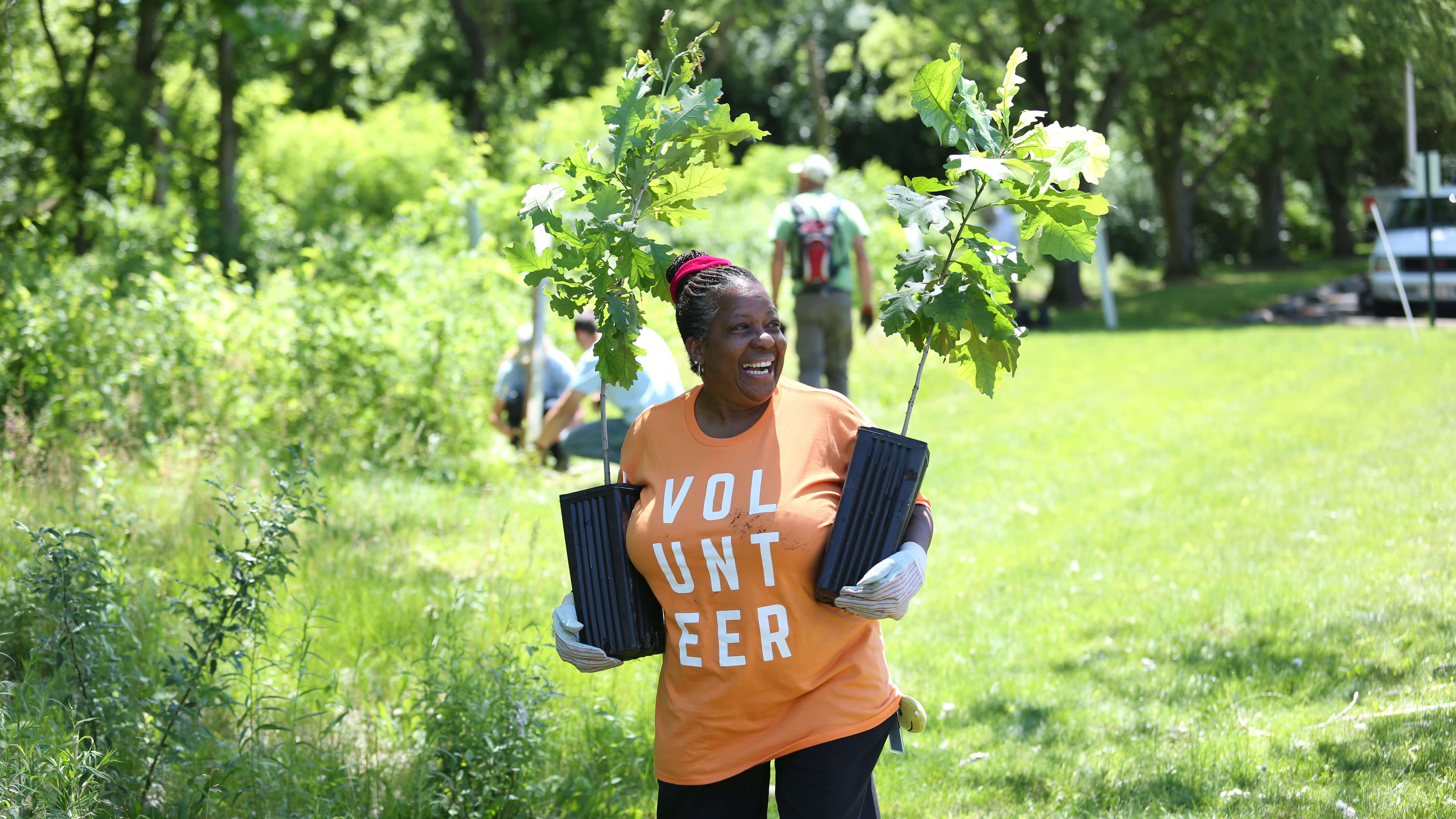 woman holding tree saplings and smiling while volunteering outdoors