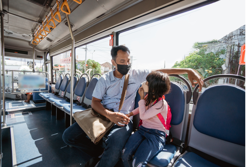 asian man riding bus with daughter to reduce carbon footprin