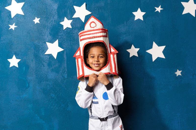 child wearing rocket helmet and space suit standing in front of starry background