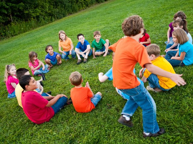 a group of children sit in a circle outside playing a game