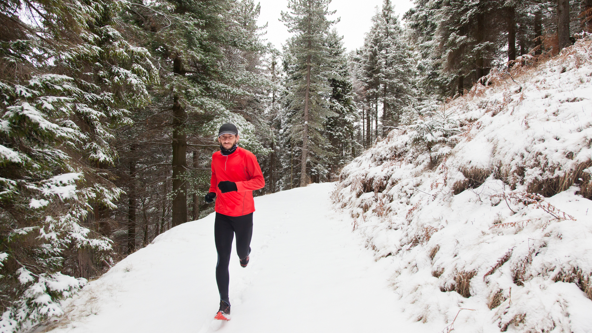 A man jogs on a trail in a snowy forest.