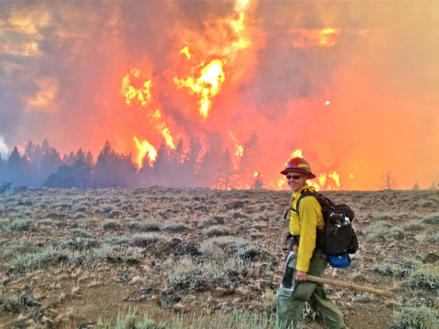 Lorena Williams standing in front of a raging fire in full firefighting gear.