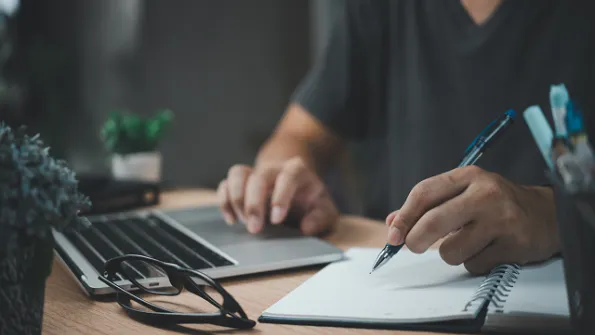 Person typing on computer while writing on a notepad