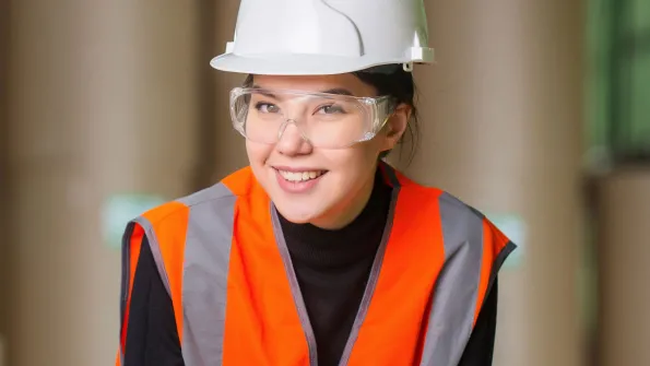 a young woman wearing a reflector vest and hard hat, employee of a manufacturing company