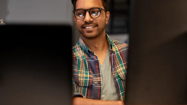 Young man with glasses smiling and looking at a computer