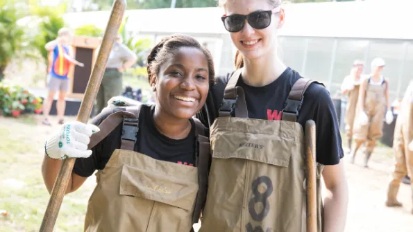 Two girls in bibs and digging equipment outdoors