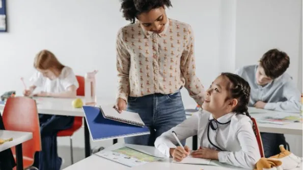a female teacher speaks with a girl student at her desk
