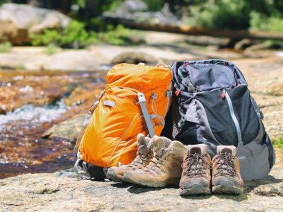 backpacks and hiking boots on a rock near water
