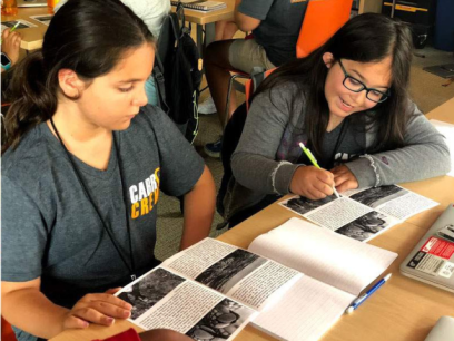 Two girls sitting at a desk looking at books together