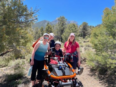 a woman site in an all terrain wheelchair surrounded by a group of people on the trail 