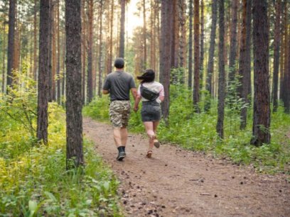 a man in camo shorts holds hands with a woman as they walk through the forest