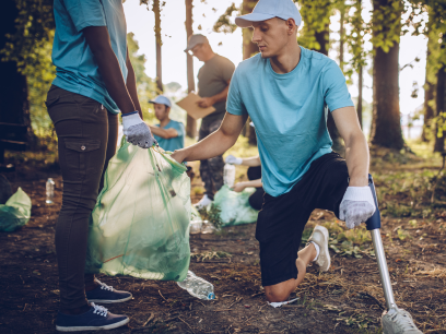 A man with an artificial leg helps pick up trash in a forested setting.