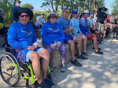 a man using a wheelchair sits with family and friends waiting for a kayak launch