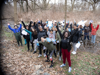 Middle school students outdoors with arms in the air and happy