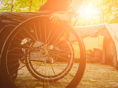 man in wheelchair next to a tent in the forest